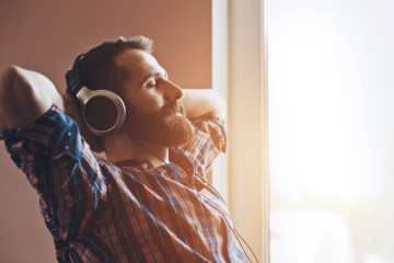 Ein Mann verschränkt die Hände hinterm Kopf während er Musik hört.