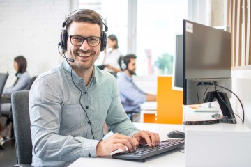 Mann vor seinem Computer im Büro, er trägt ein Headset