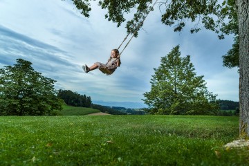 Mädchen schwingt auf einer Schaukel, die an einem Baum befestigt ist.