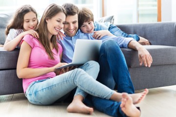 Familie mit Laptop auf und vor dem Sofa