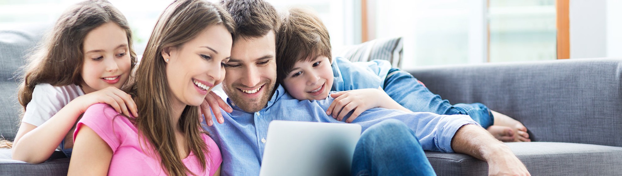 Familie mit Laptop auf und vor dem Sofa