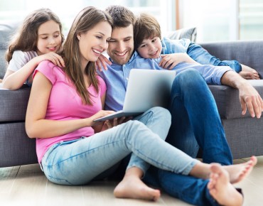 Familie mit Laptop auf und vor dem Sofa