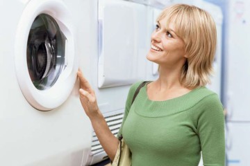 Frau steht vor einer Waschmaschine und sieht ins Innere