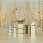 Urne steht in einer Schale auf einem goldenen Podest, dahinter Weidenäste an den Wänden