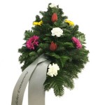 grüner Bukett Kranz mit zwei weißen Nelken, zwei roten Tulpen, zwei magenta-farbene Gerbera und zwei gelbe Gerbera. Weiße Schleife mit verschnörkeltem Schriftzug "in Erinnerung" grüner Bukett Kranz mit zwei weißen Nelken, zwei roten Tulpen, zwei magenta-farbene Gerbera und zwei gelbe Gerbera. Weiße Schleife mit verschnörkeltem Schriftzug "in Erinnerung"