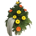 grüner Bukett Kranz mit fünf gelben Gerbera und vier orangene Gerbera. Weiße Schleife mit verschnörkeltem Schriftzug. grüner Bukett Kranz mit fünf gelben Gerbera und vier orangene Gerbera. Weiße Schleife mit verschnörkeltem Schriftzug.