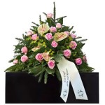 grünes Bukett mit rosa Rosen und grün-rosa Calla mit weißer Schleife steht auf schwarzem Podest grünes Bukett mit rosa Rosen und grün-rosa Calla mit weißer Schleife steht auf schwarzem Podest