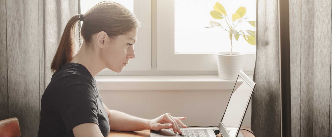 Frau sitzt vor Laptop mit Block und Stift vor sich