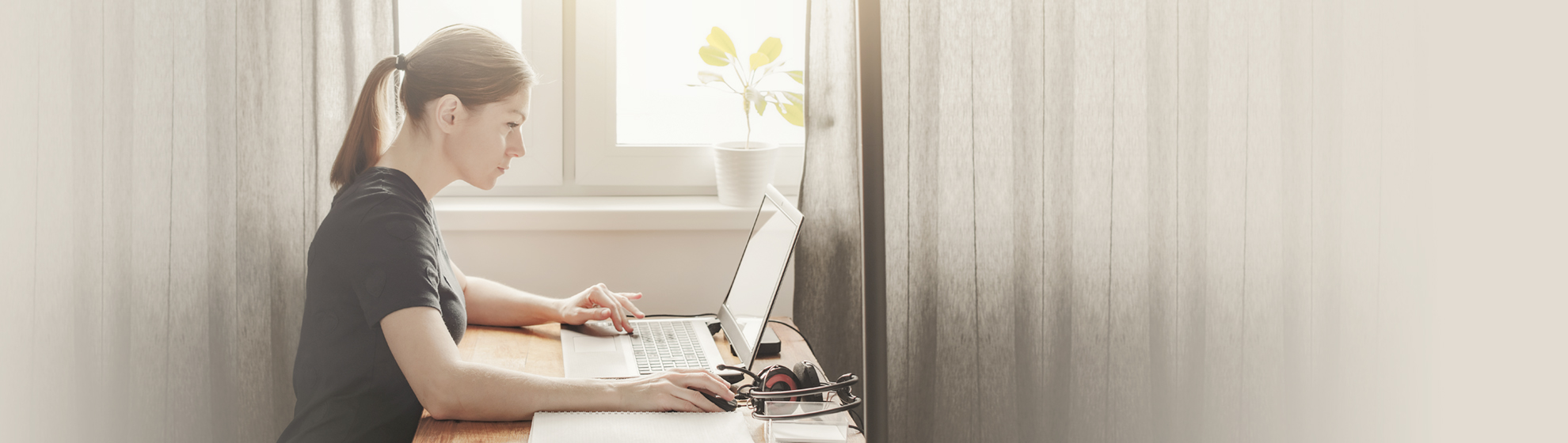 Frau sitzt vor Laptop mit Block und Stift vor sich