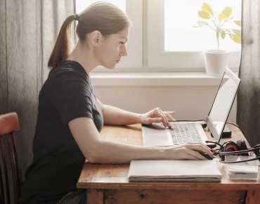 Frau sitzt vor Laptop mit Block und Stift vor sich