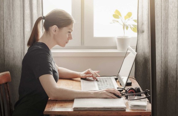 Frau sitzt vor Laptop mit Block und Stift vor sich