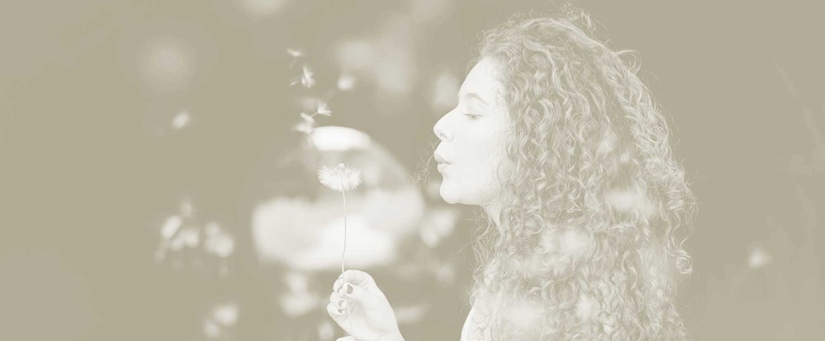 junge Frau pustet eine Pusteblume in den Wind
