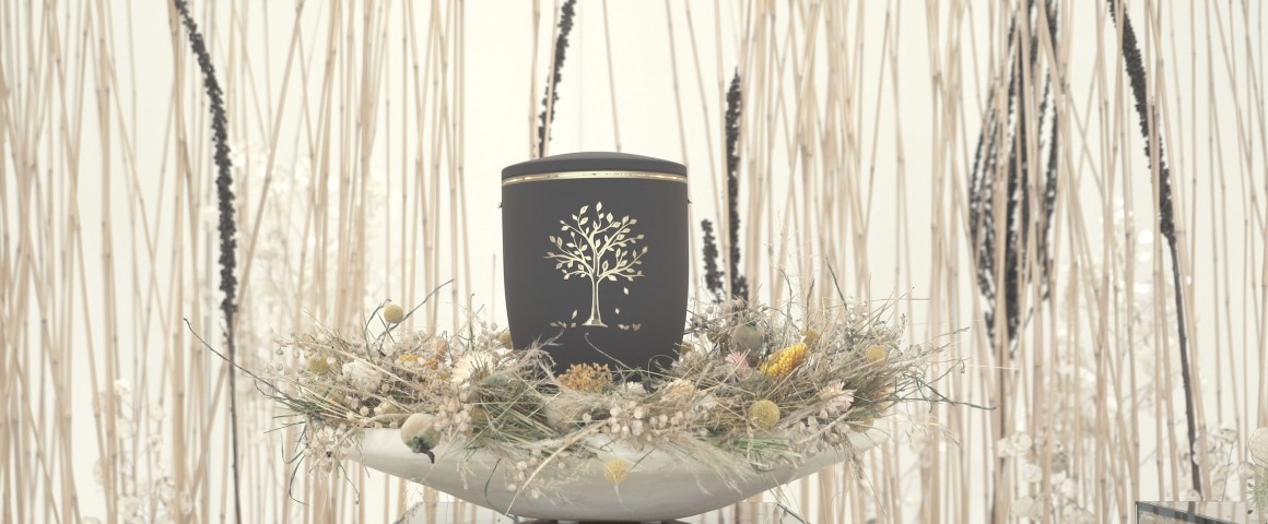 graue Urne steht in einer Schale mit Trockenblumen dekoriert