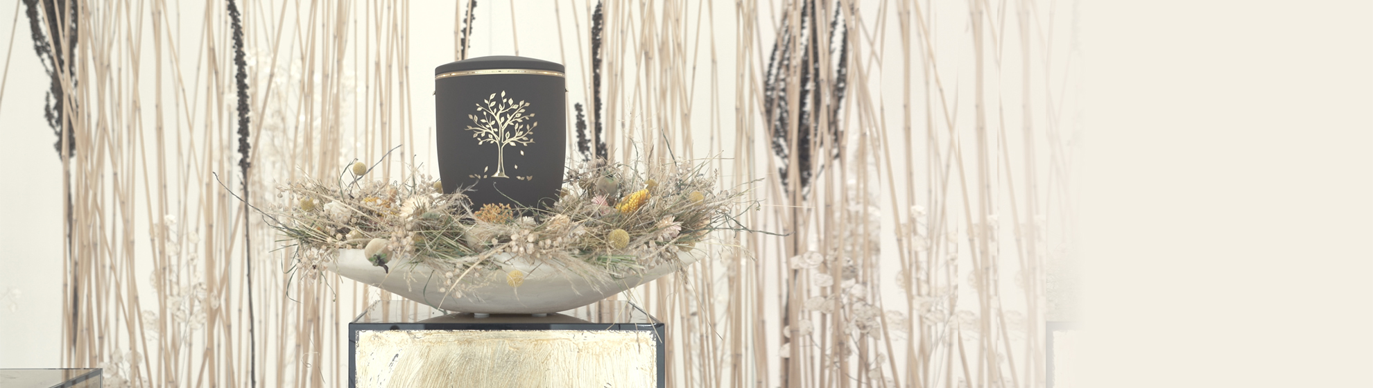 graue Urne steht in einer Schale mit Trockenblumen dekoriert