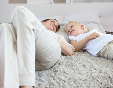 Kind und Frau liegen mit Polster auf Teppich 