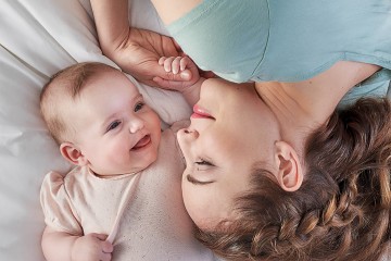 Eine Frau liegt mit ihrem Baby im Bett, sie lächeln sich an