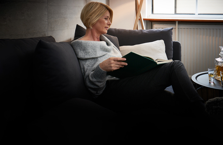 Eine Frau sitzt auf der Couch und liest in einem Buch