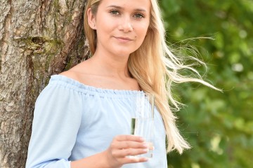 Frau lehnt mit Wasserglas in der Hand an Baum